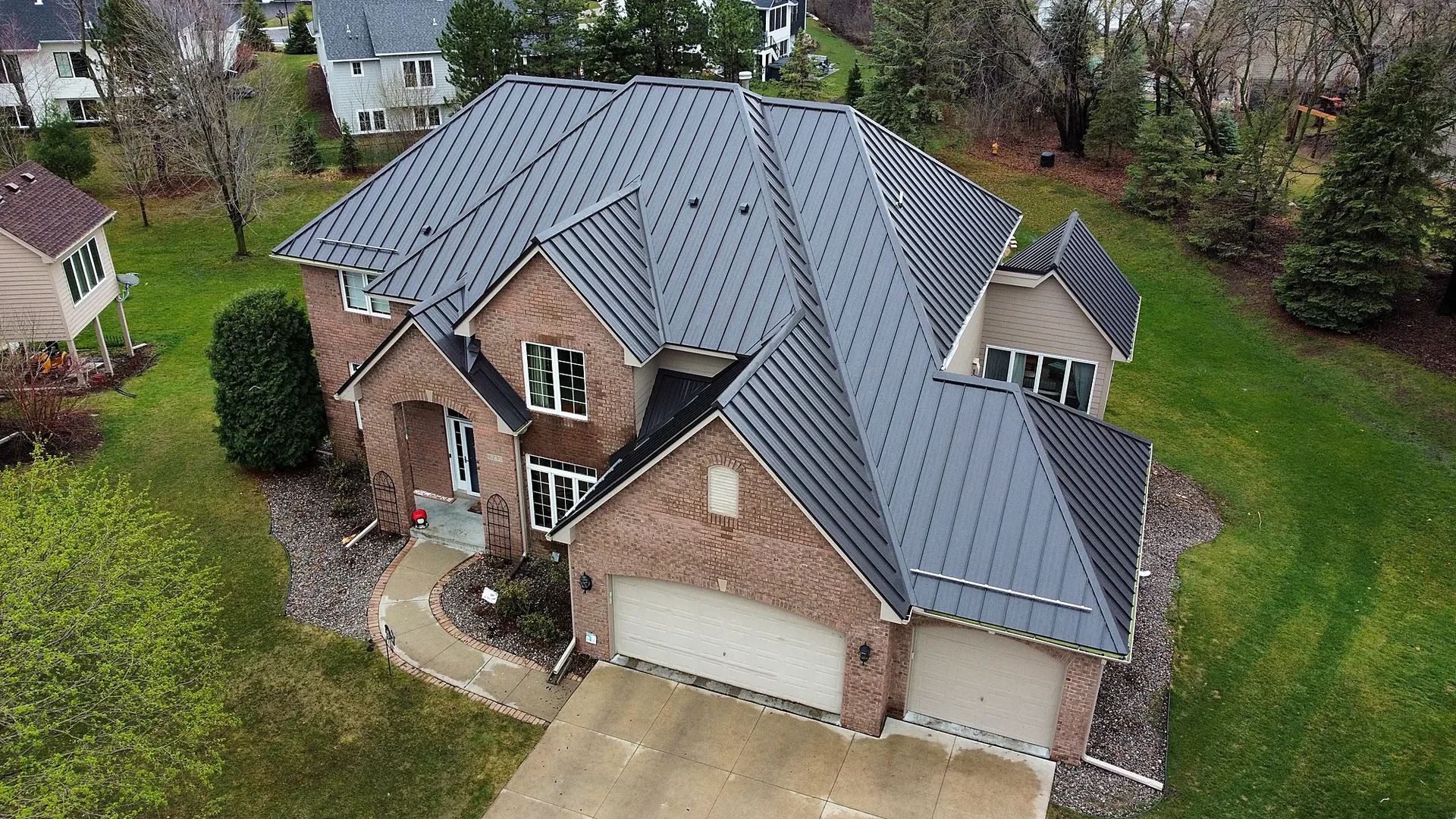 Aerial view of a brick two-story home with a dark standing seam metal roof in Minnesota